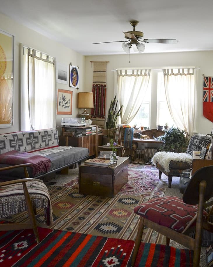 Eclectic living room with patterned rugs, vintage furniture, wall art, and a ceiling fan.