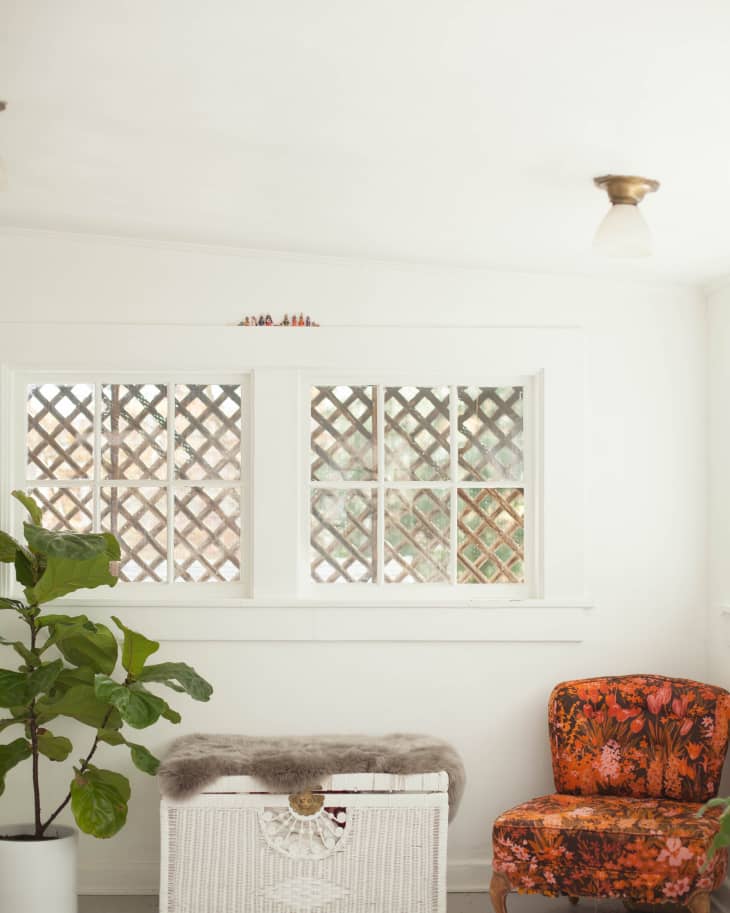 Sunroom with a potted plant, white wicker chest with fur cover, and an orange floral chair.