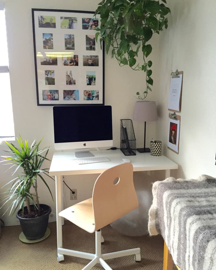 Home office with a white desk, computer, wooden chair, hanging plant, framed photos, and a potted plant.
