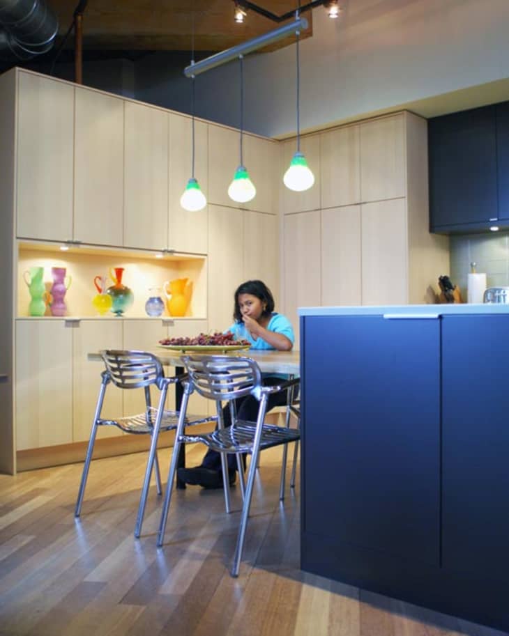 Child eating at a kitchen table with colorful vases on display shelves and modern pendant lights above.