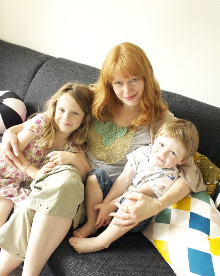Woman with red hair sitting on a dark sofa with two children, surrounded by colorful pillows.