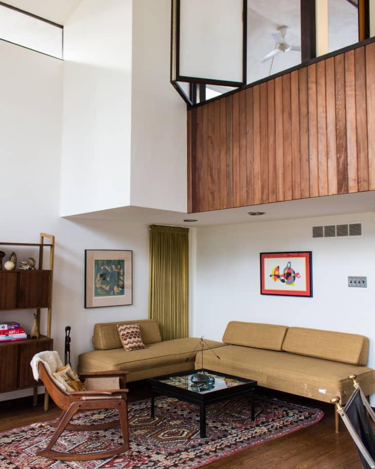 Mid-century modern living room with tan sectional sofa, wooden chair, glass coffee table, and patterned rug.