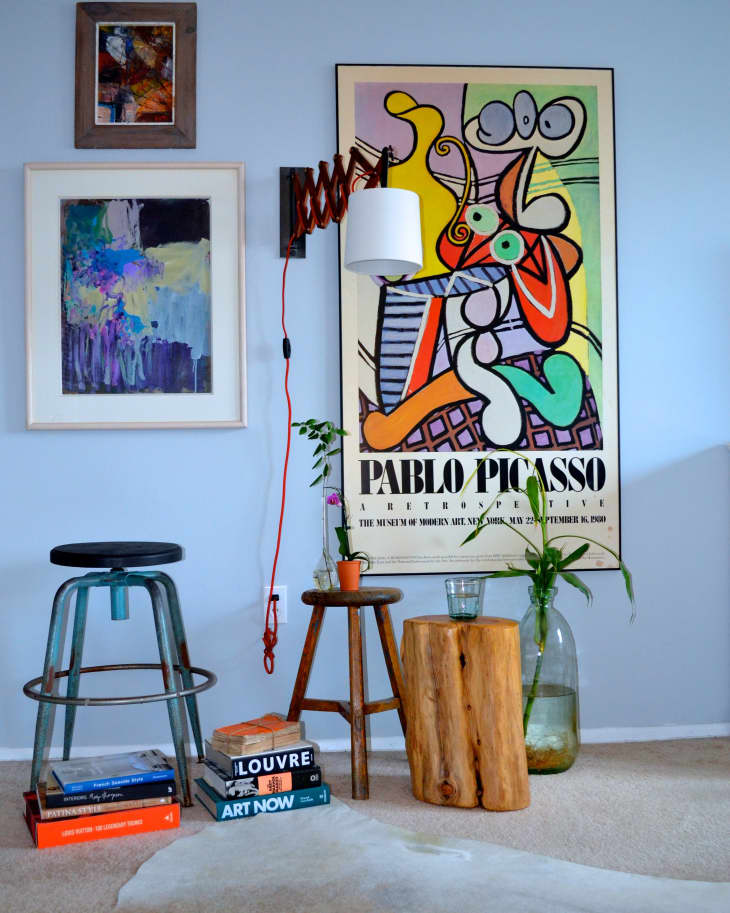 Eclectic room with Picasso poster, abstract art, stools, books, and a wooden log table with plants.
