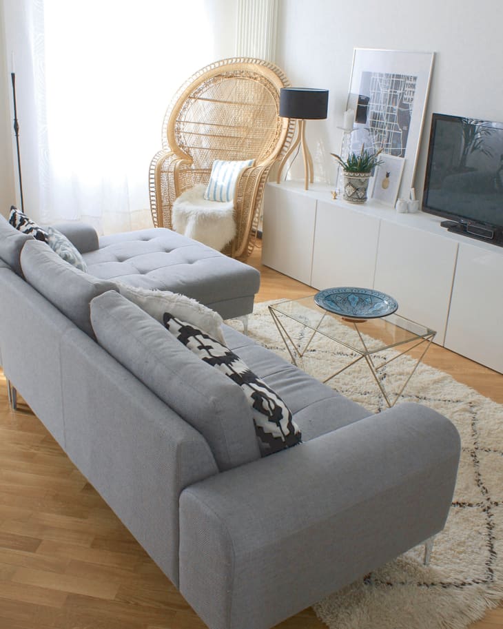 Living room with a gray sofa, wicker chair, glass table, TV, and decor on a white cabinet.
