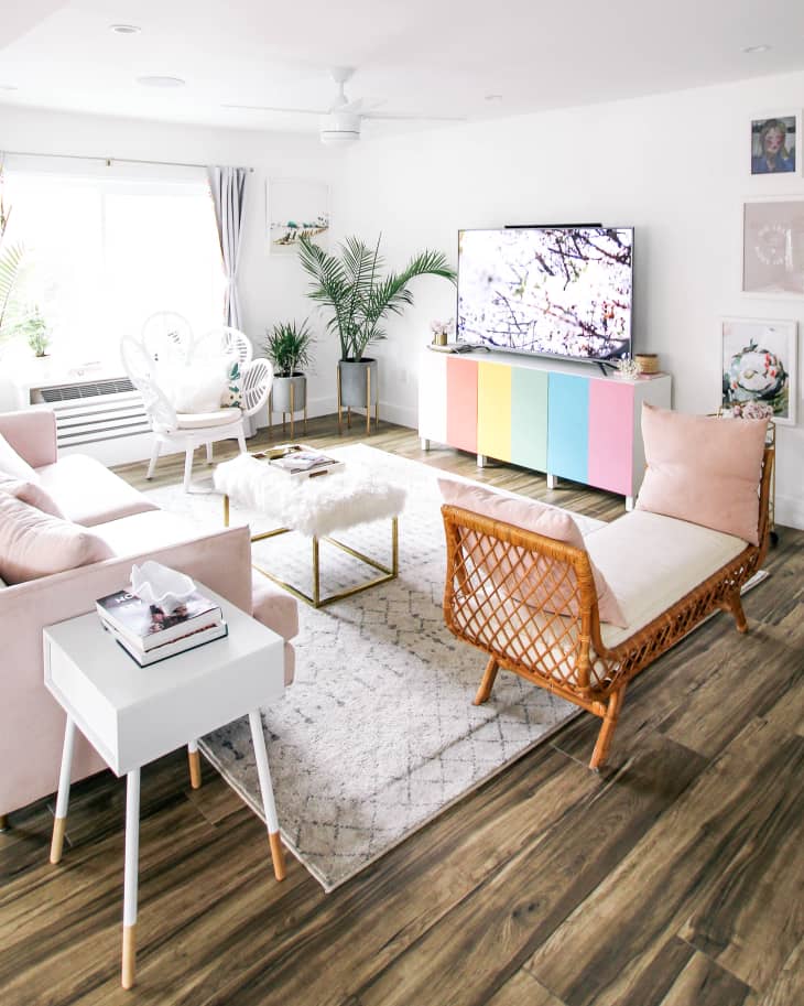 Bright living room with pastel furniture, a pink sofa, wicker chair, colorful TV stand, and framed wall art.