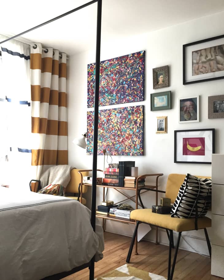 Bedroom with colorful abstract art, yellow chairs, striped curtains, and a wooden desk with books and decor.