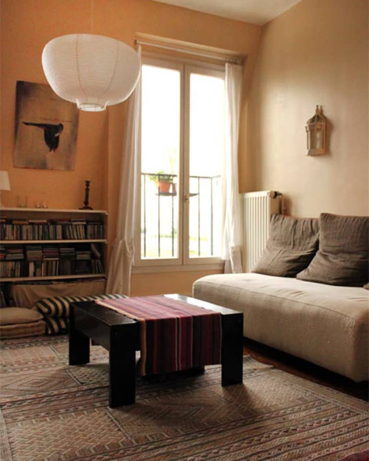 Cozy living room with a beige sofa, black coffee table, striped runner, bookshelf, and large window with sheer curtains.