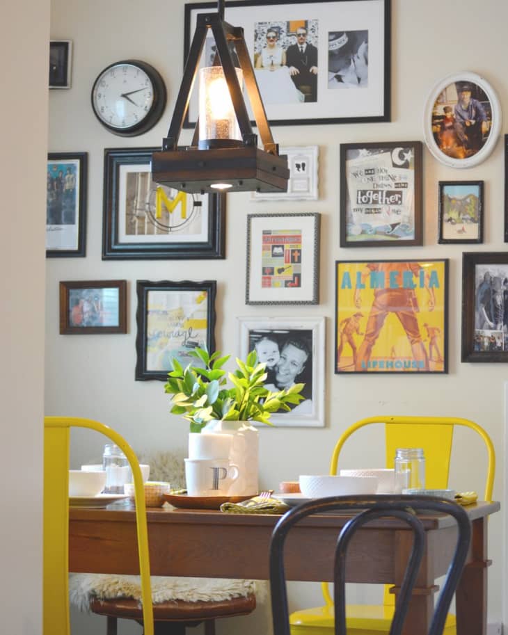 Dining area with yellow chairs, wooden table, potted plant, and a gallery wall of framed art and photos.
