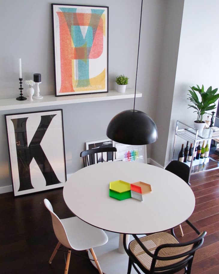 Dining area with round white table, mixed chairs, colorful wall art, and a black pendant light.
