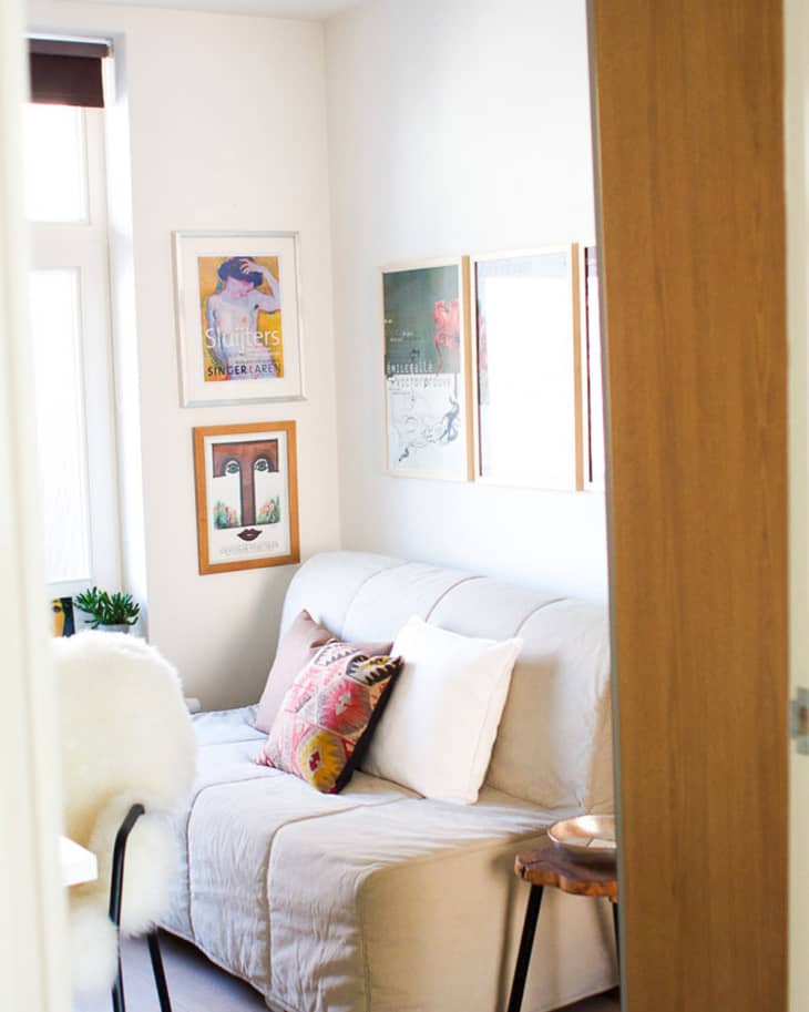 Cozy living room with a beige sofa, colorful cushions, wall art, and a small wooden side table.
