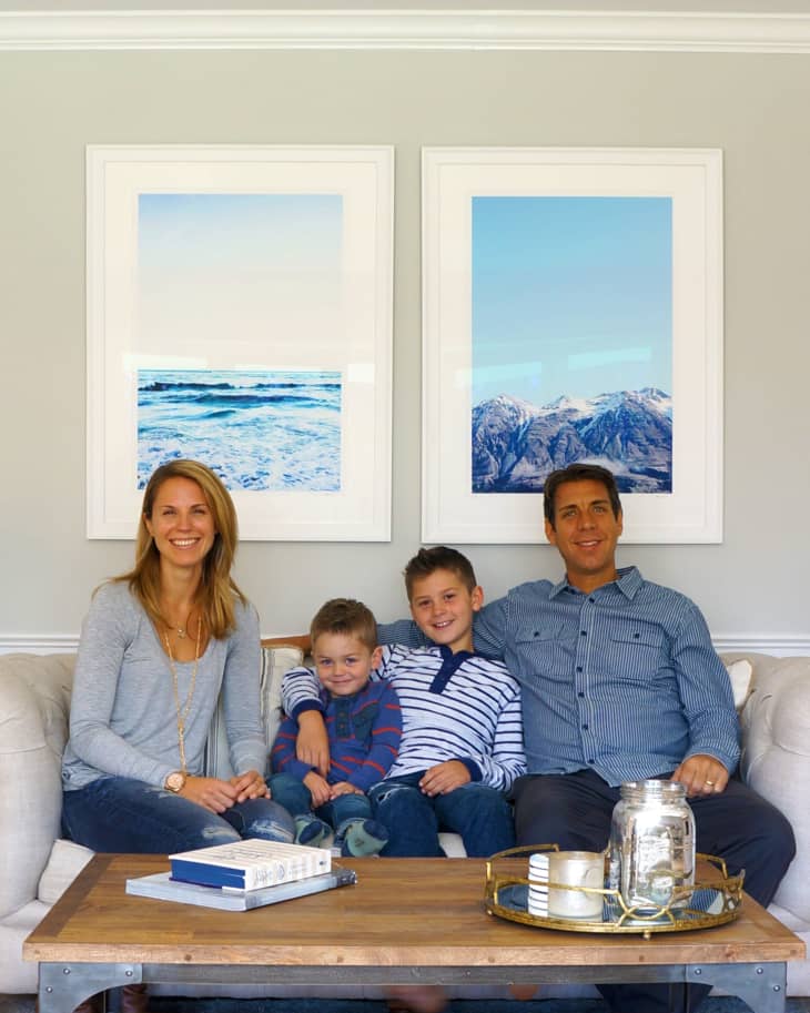 Family of four sitting on a beige sofa in a living room with ocean and mountain artwork on the wall.