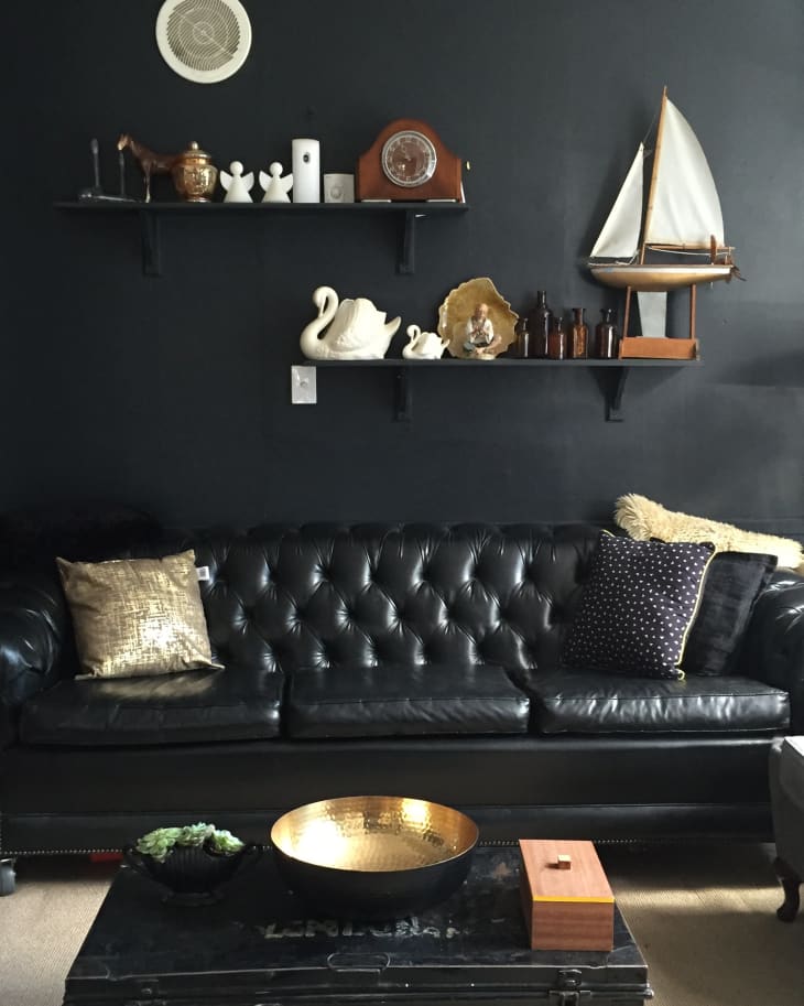 Black leather tufted sofa with gold and polka dot pillows, nautical decor, and shelves with various ornaments.
