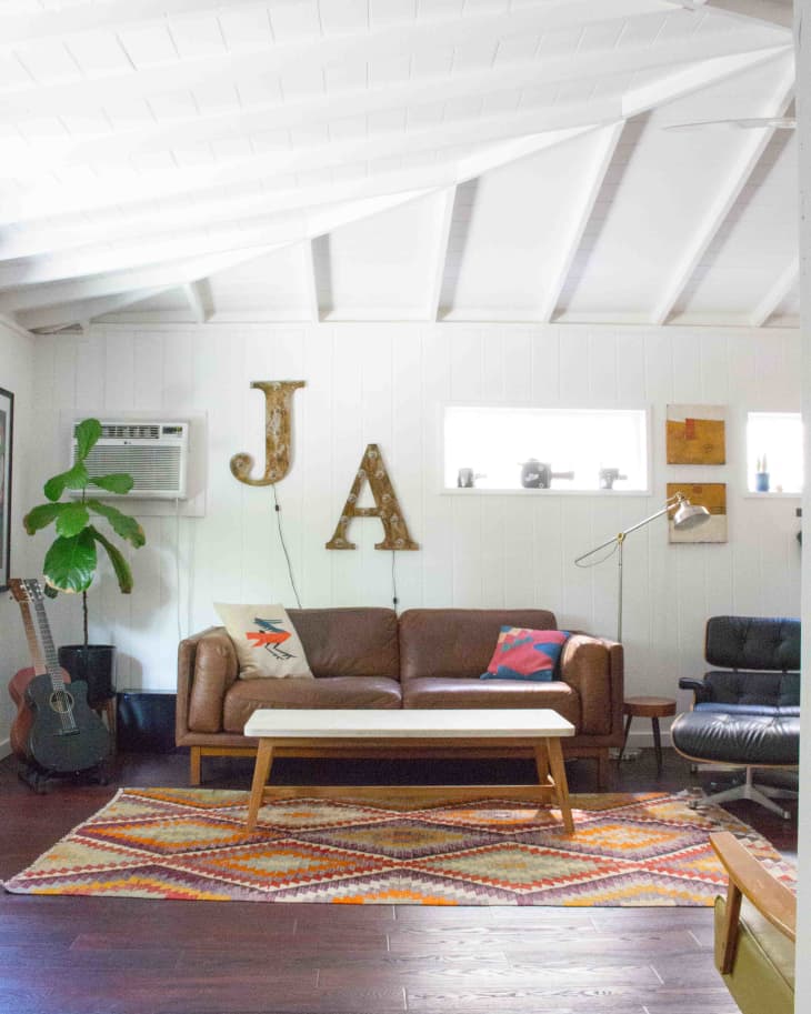 Living room with brown leather sofa, colorful pillows, patterned rug, guitar, and large letters "J" and "A" on the wall.