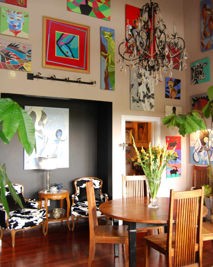 Dining room with wooden table, chairs, chandelier, colorful wall art, and black-and-white patterned chairs.