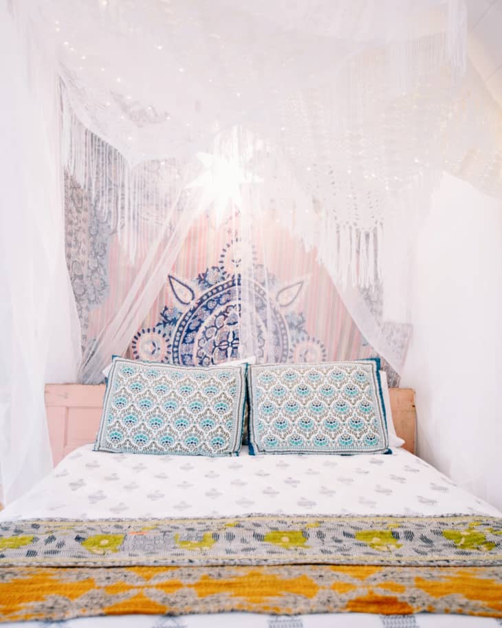 Bohemian bedroom with patterned pillows, tapestry, and canopy over a white bedspread.