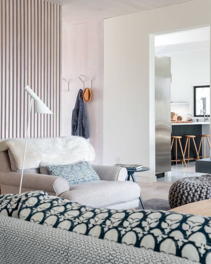 Cozy living room with a gray armchair, patterned cushions, and a white floor lamp, leading to a modern kitchen.