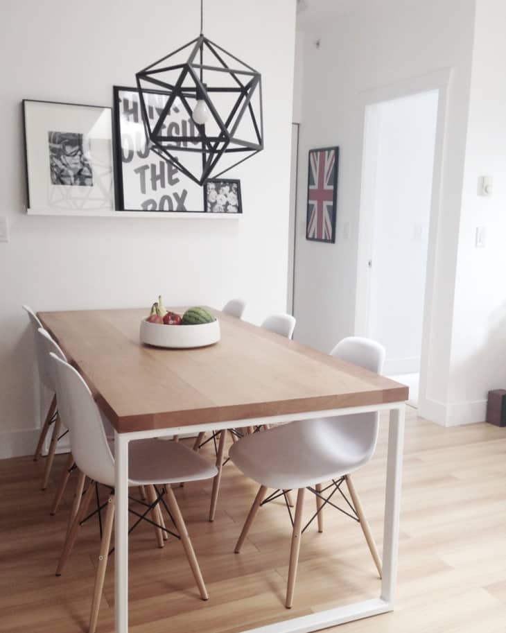 Dining room with a wooden table, white chairs, geometric pendant light, and framed wall art.