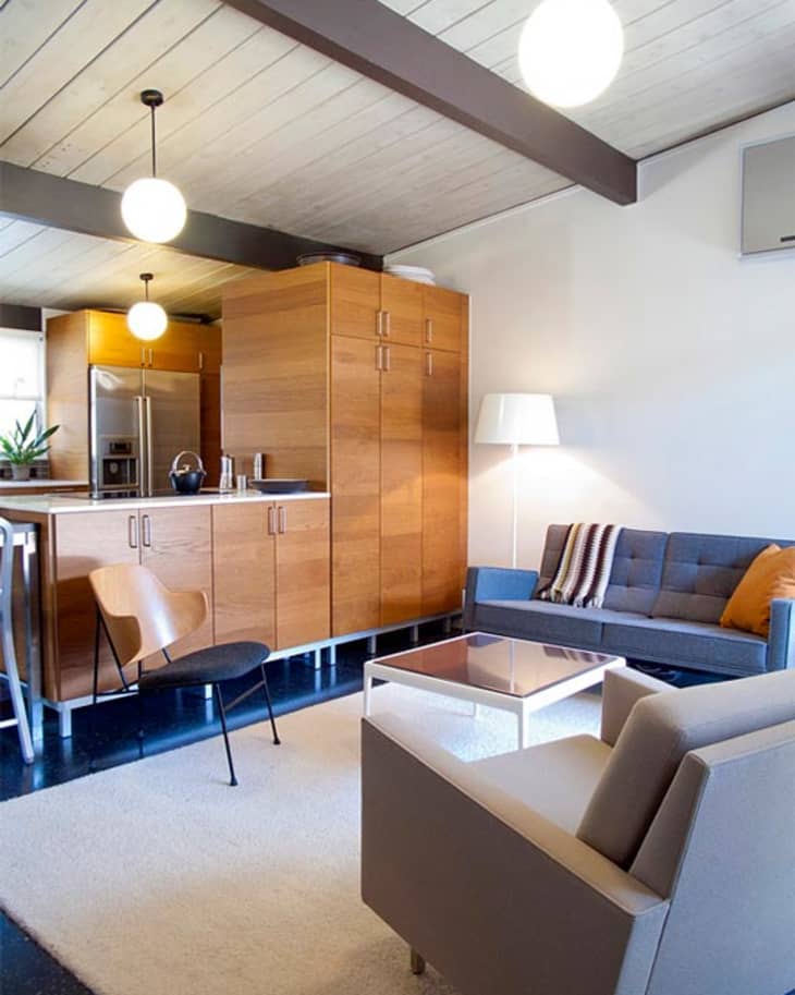 Mid-century modern living room with wooden cabinets, gray sofa, beige armchair, and pendant lights.