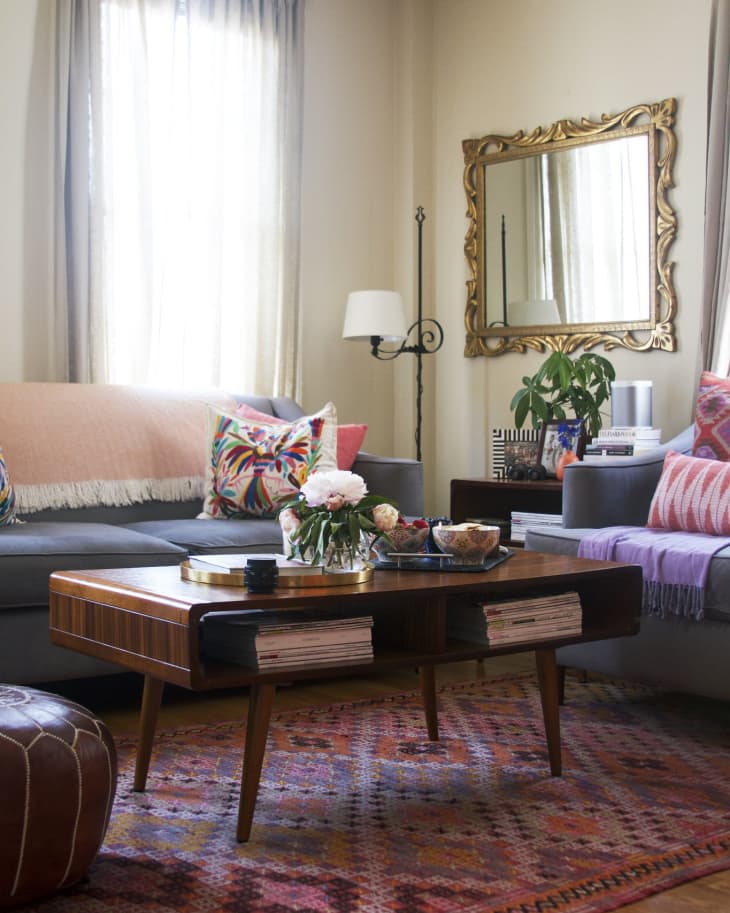 Cozy living room with gray sofas, colorful pillows, wooden coffee table, ornate mirror, and patterned rug.
