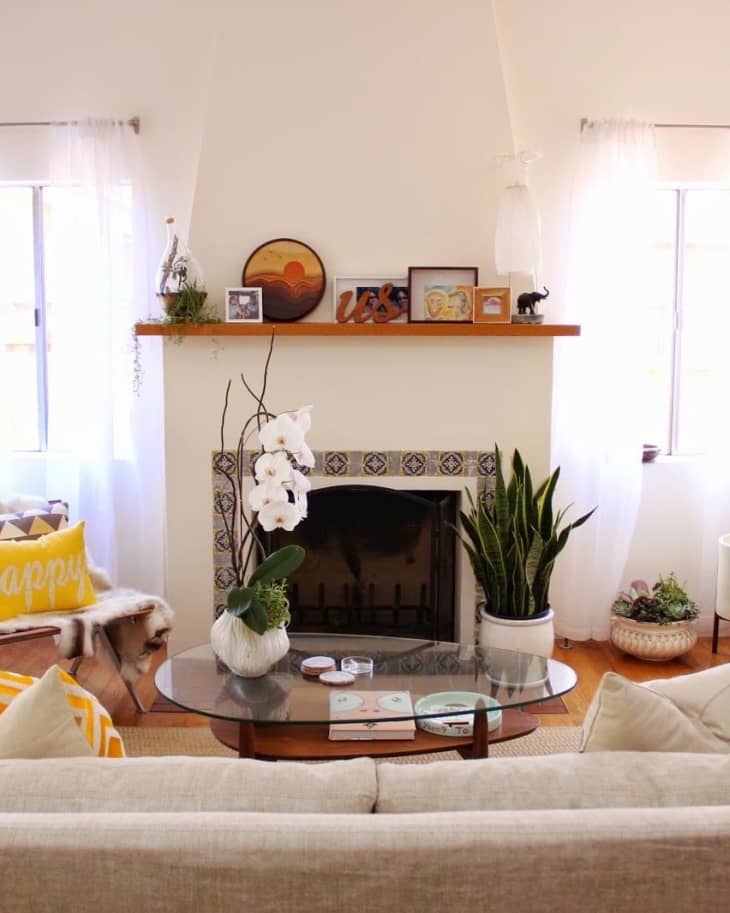 Living room with a tiled fireplace, glass coffee table, orchid, snake plant, and decor on the mantel.