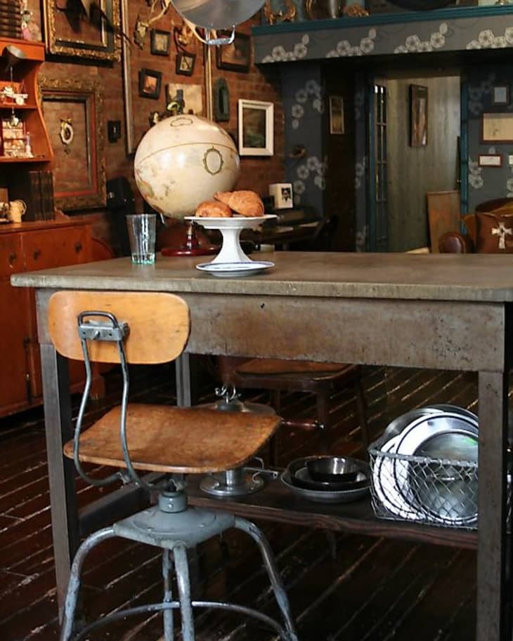 Vintage kitchen with wooden chair, metal table, globe, framed art, and pastries on a cake stand.