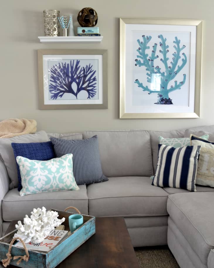 Gray sectional sofa with blue and white pillows, coral artwork, and a wooden coffee table with a decorative tray.