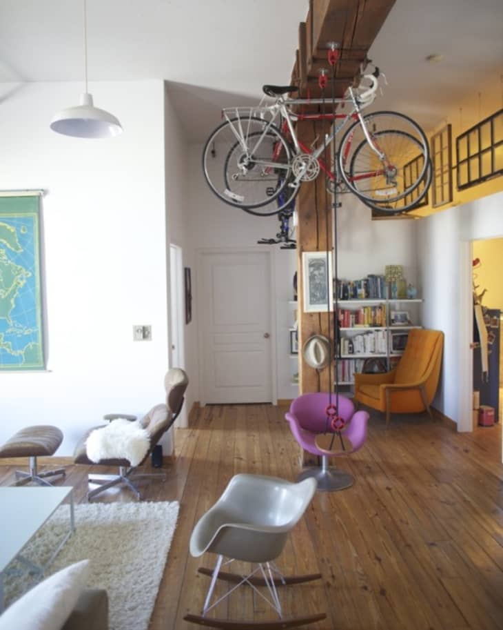 Living room with hanging bicycles, wooden floors, colorful chairs, bookshelf, and a world map on the wall.