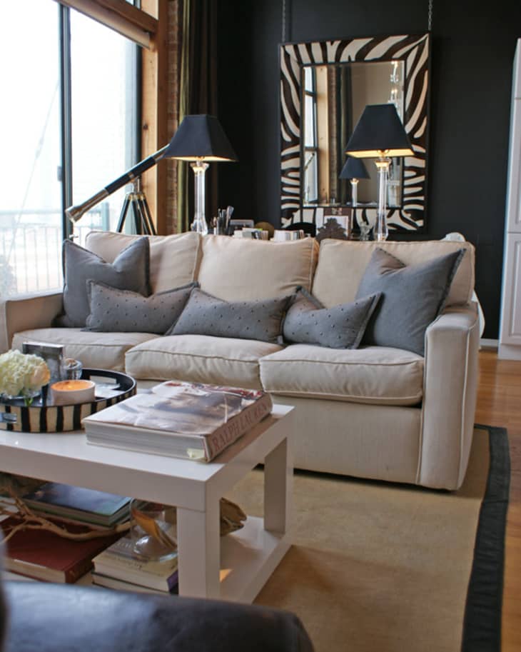 Living room with cream sofa, gray pillows, zebra-striped mirror, black lamps, and a white coffee table with books and decor.