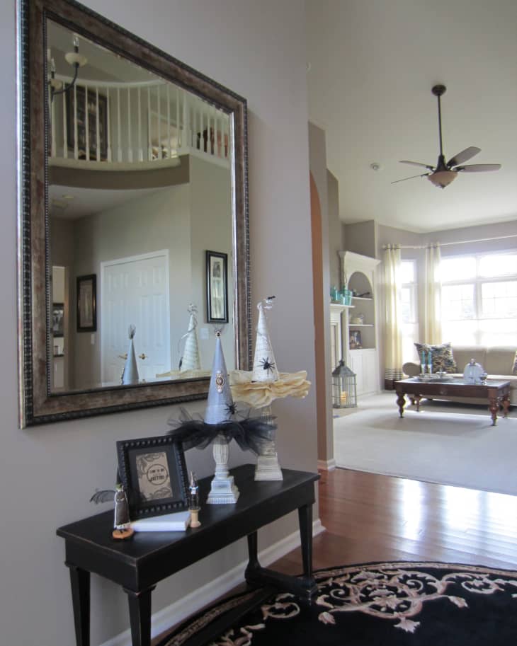 Hallway with large mirror, decorative witch hats on a table, and view into a living room with a ceiling fan and coffee table.