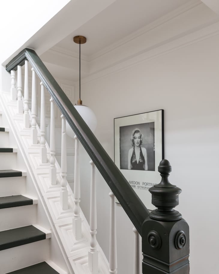 Staircase with black handrail, white balusters, a pendant light, and a framed black-and-white portrait on the wall.