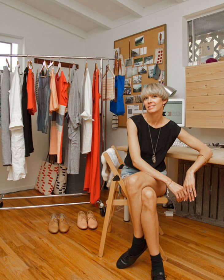 Woman sitting in a home office with a clothing rack, shoes, and a corkboard with photos.