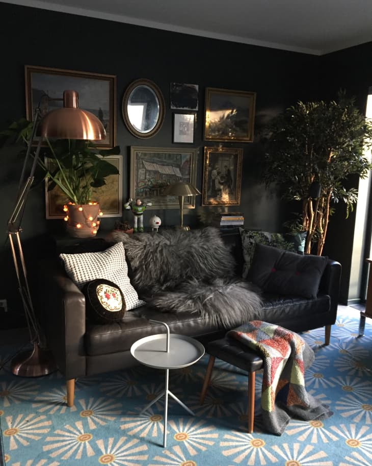 Cozy living room with dark sofa, fluffy pillows, eclectic art, copper lamp, and blue patterned rug.