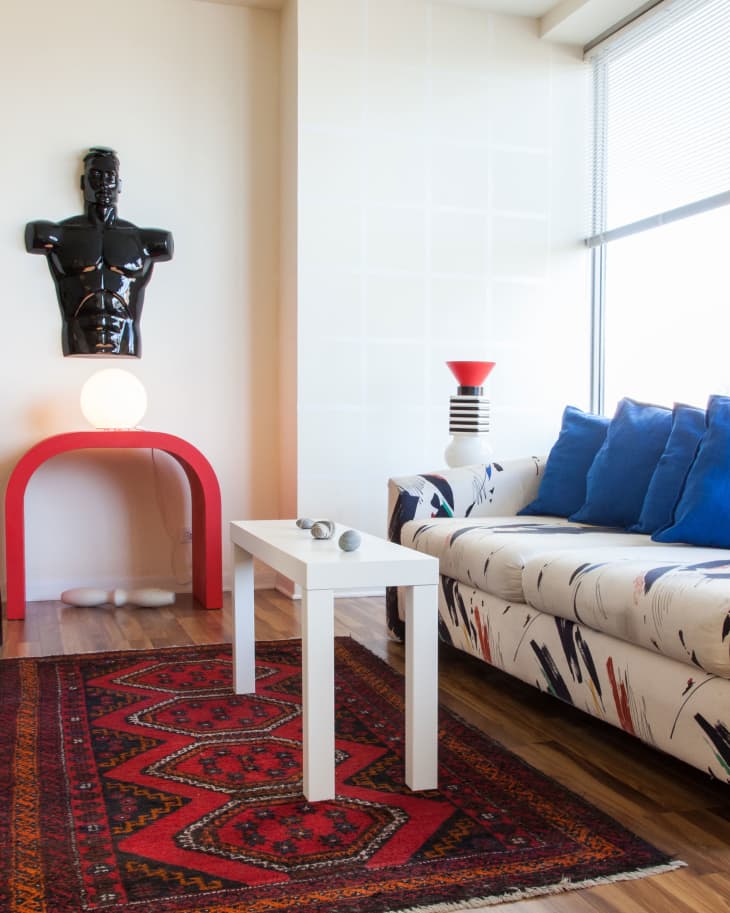 Living room with abstract sofa, red patterned rug, white table, and black torso sculpture on wall.