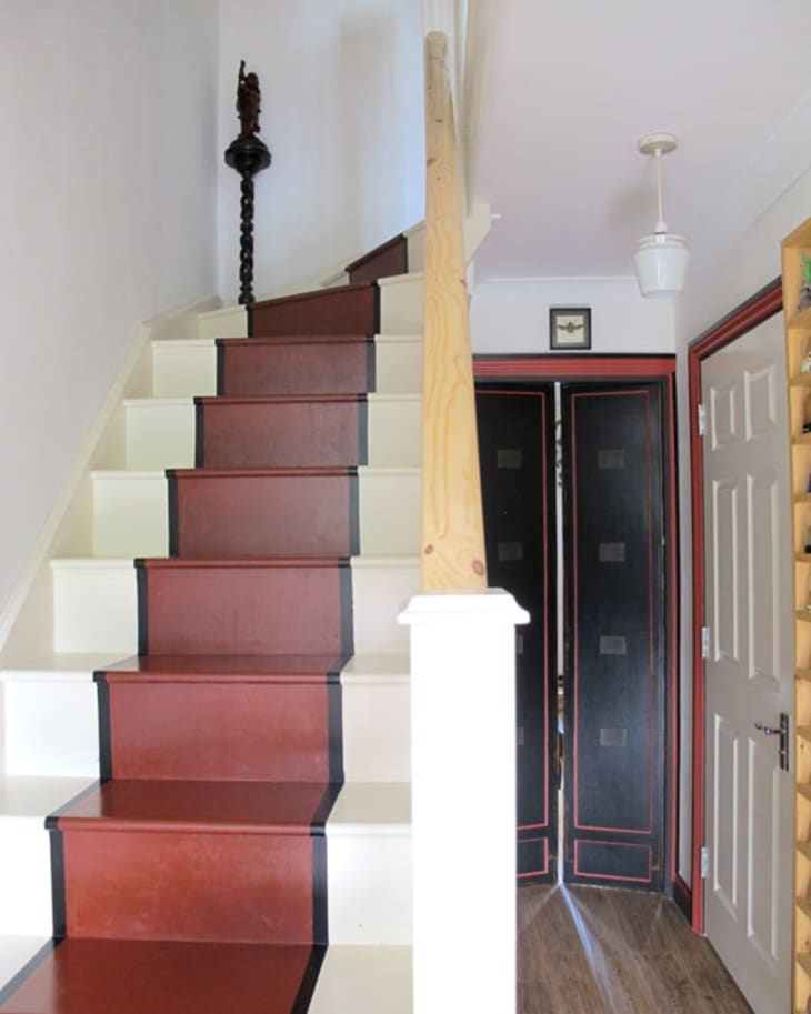Red and white staircase with black trim, wooden handrail, and a decorative statue on the landing.