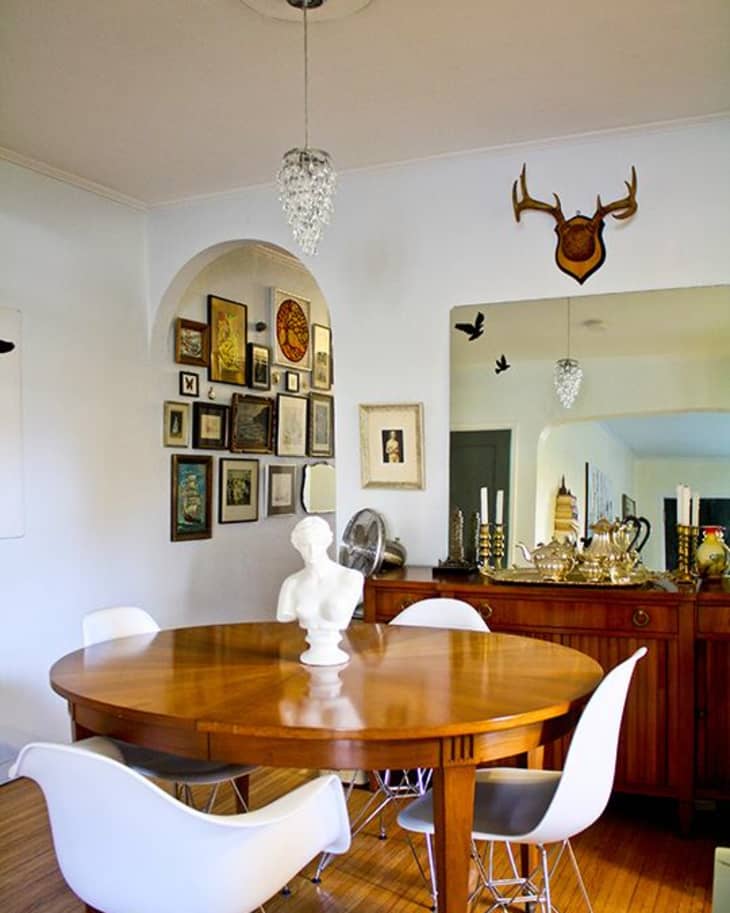 Dining room with round wooden table, white chairs, wall art, chandelier, and decorative bust centerpiece.