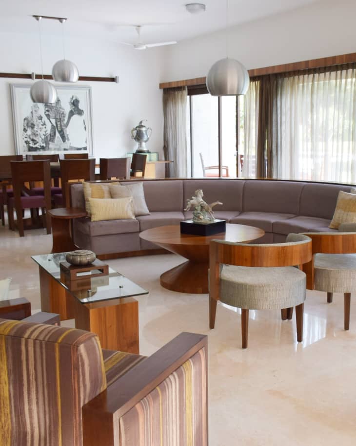 Modern living room with a curved sofa, round wooden table, striped armchair, and pendant lights, leading to a dining area.