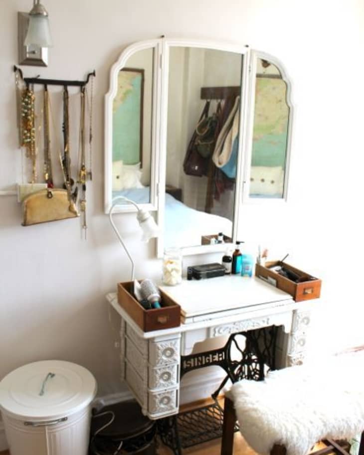 White vintage vanity with mirror, jewelry rack, and stool with fur cover in a bedroom corner.