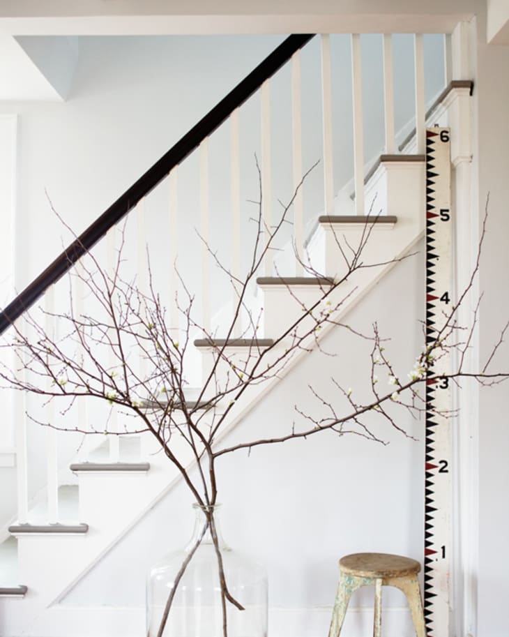 Staircase with white railing, large glass vase with branches, and a rustic stool on wooden floor.
