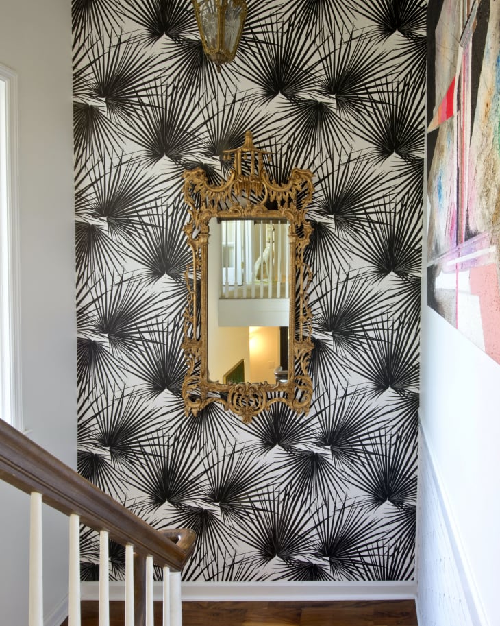 Hallway with black and white palm leaf wallpaper, ornate gold mirror, and hanging lantern.