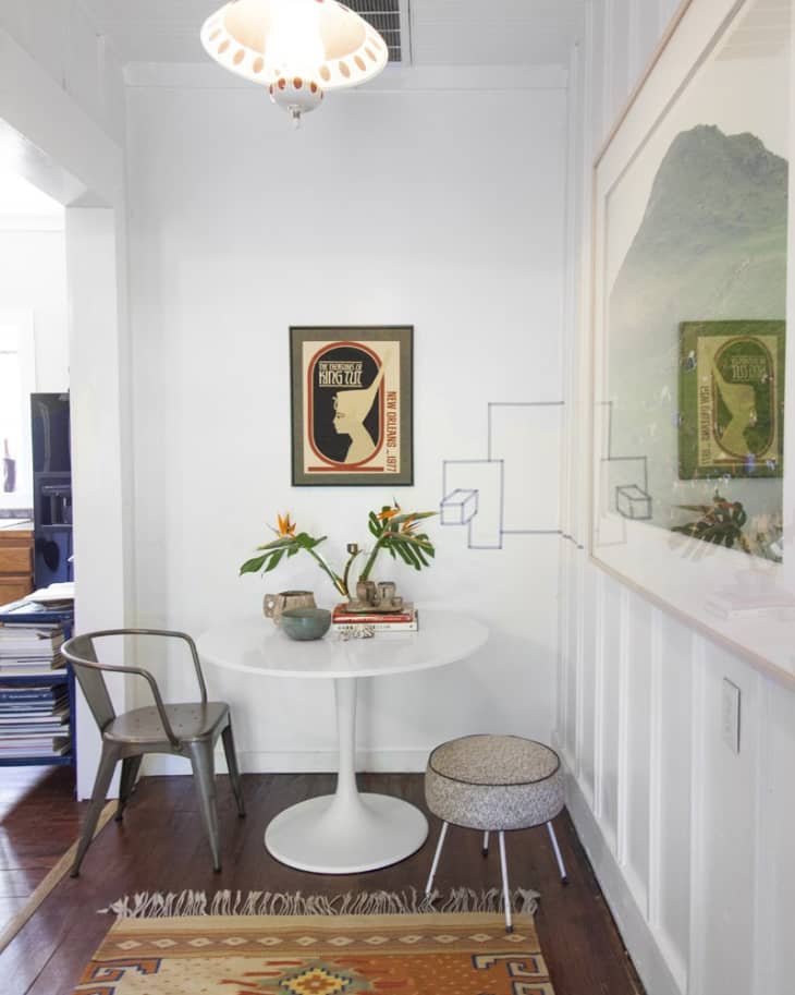 Small nook with a white round table, metal chair, stool, and bird of paradise flowers in vases.