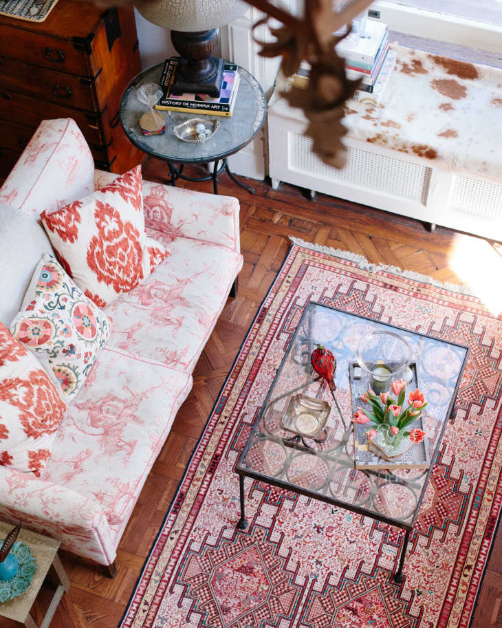 Living room with pink patterned sofa, glass coffee table, floral rug, and decorative pillows.