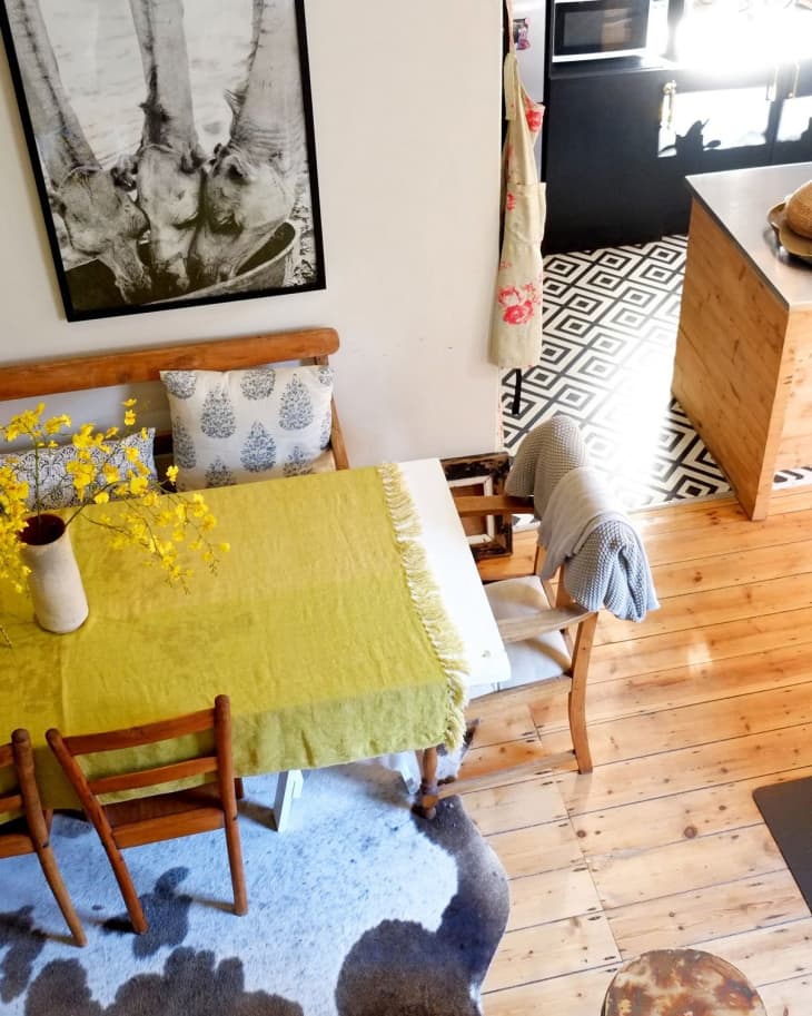 Dining area with wooden chairs, green tablecloth, yellow flowers, and a black-and-white animal photo on the wall.