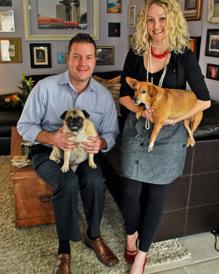 Man and woman smiling with two dogs in a living room with framed art.