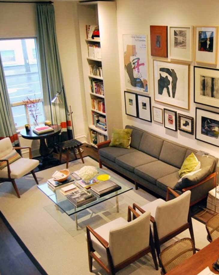 Cozy living room with gray sofa, armchairs, glass coffee table, bookshelves, and framed art on walls.