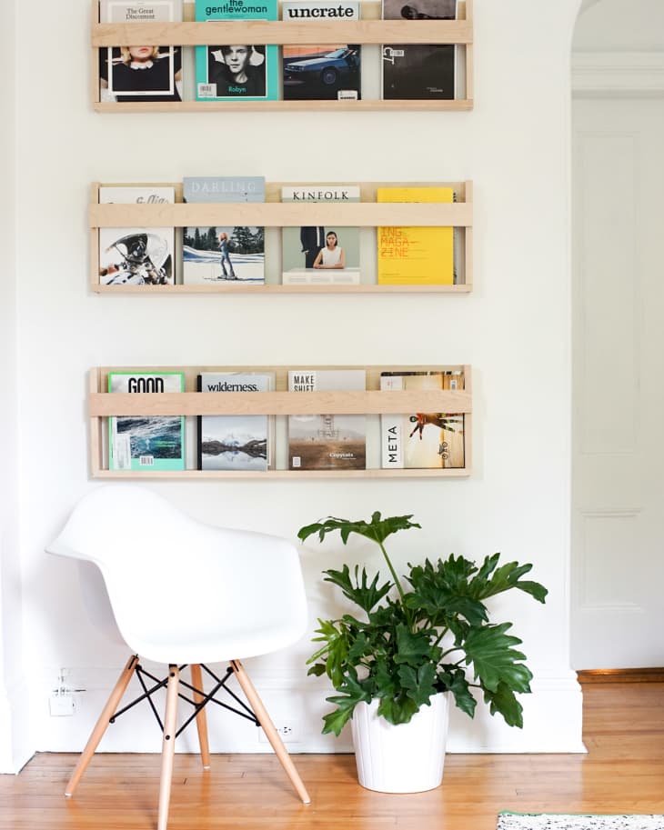 White chair and potted plant beside wall-mounted wooden magazine racks displaying various colorful magazines.
