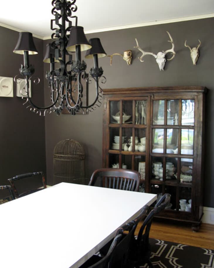 A dining room with animal skulls on the wall and a black chandelier above the table.