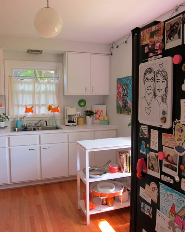 Bright kitchen with white cabinets, a small island, and a fridge covered in drawings and magnets.