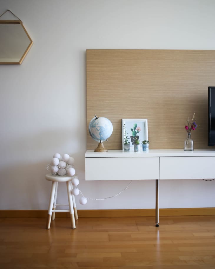 Modern living room with a white console table, globe, framed art, small plants, and a stool with string lights.