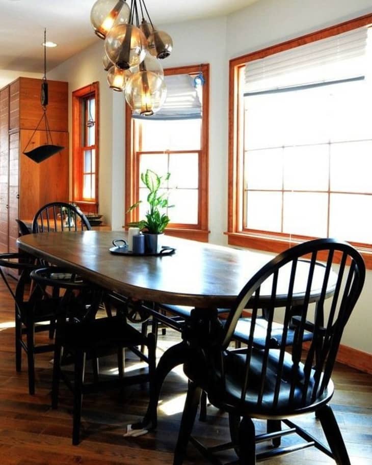 Dining room with wooden table, black chairs, pendant lights, and large windows.