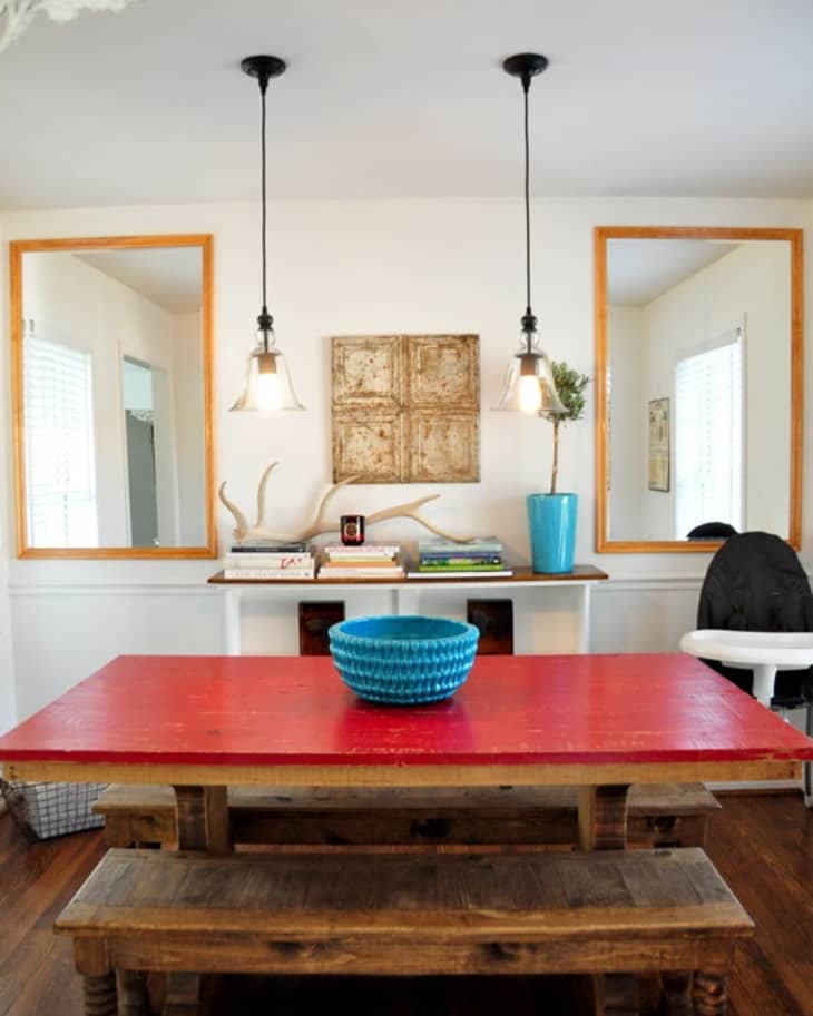 Red dining table with wooden benches, blue bowl centerpiece, pendant lights, and decorative mirrors.